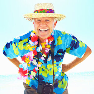 a elderly man in a colorful shirt and wearing a straw hat smiling with his hands on his hips and a camera around his neck