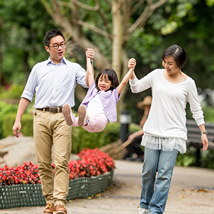 a man and a woman swinging a young child off the ground between them with a garden behind them