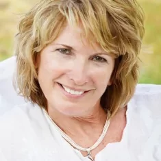 a woman with blonde short hair wearing a white shirt with a sparkly necklace smiling