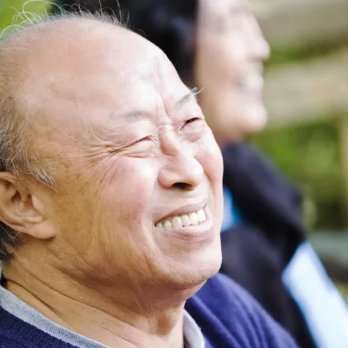 an elderly Asian couple smiling with only the gentleman in focus