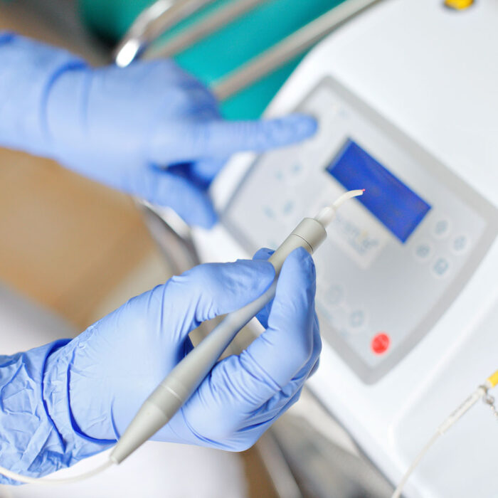 Dentist hands with blue gloves on using a Dental Diode Laser in a dental clinic.