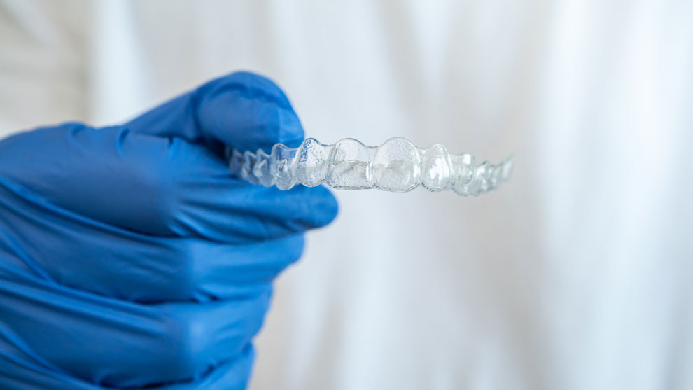 Doctor's hand with blue gloves holding invisible Invisalign orthodontic removable braces.